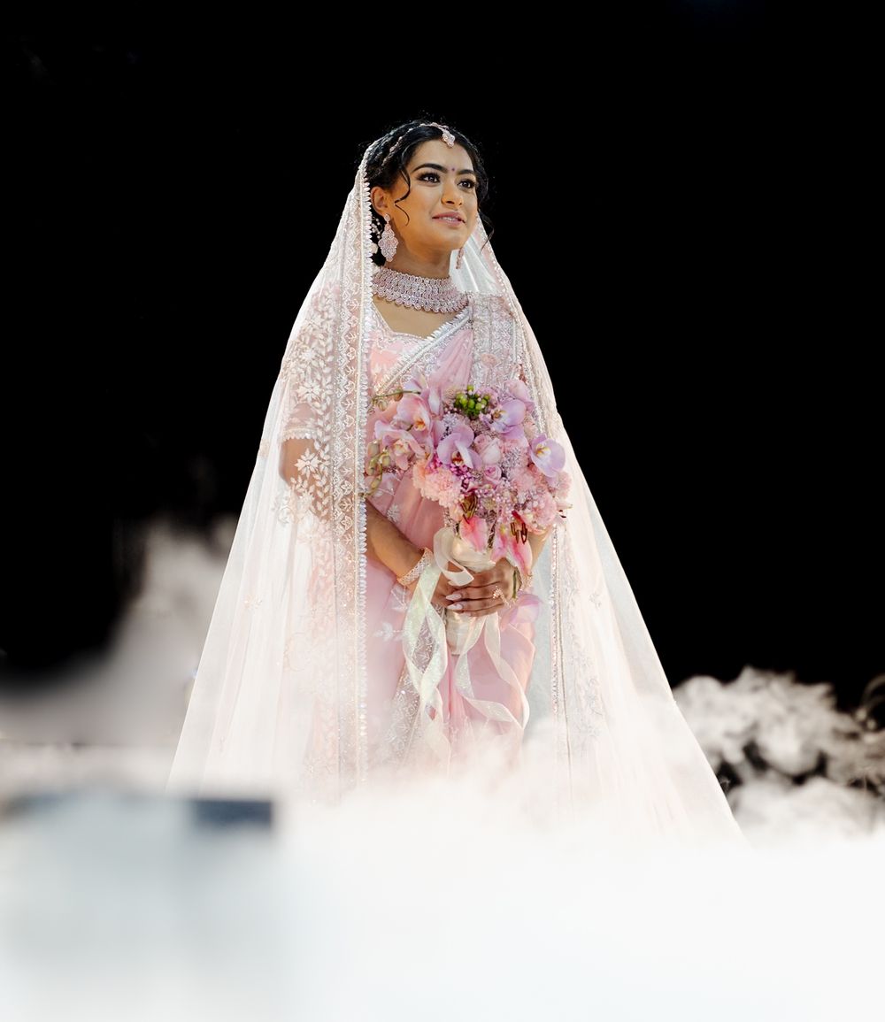 A bride in a white lace veil and gown holds a pink floral bouquet during a wedding ceremony.