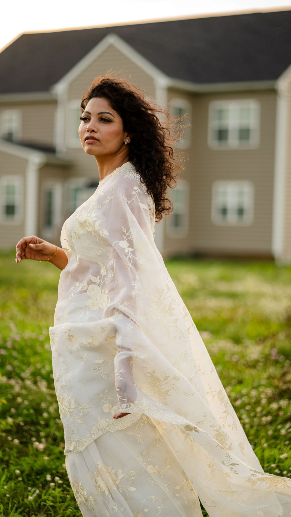 A figure in a flowing white dress twirls gracefully in a grassy field with suburban houses in the background.
