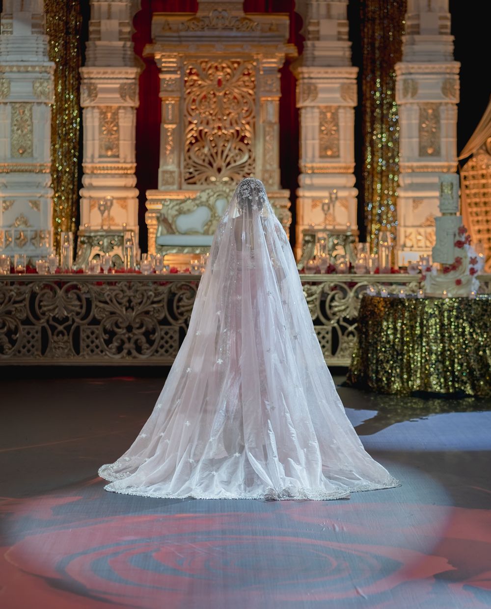 A flowing white lace wedding veil displayed in an ornate venue with decorative columns and dramatic lighting.