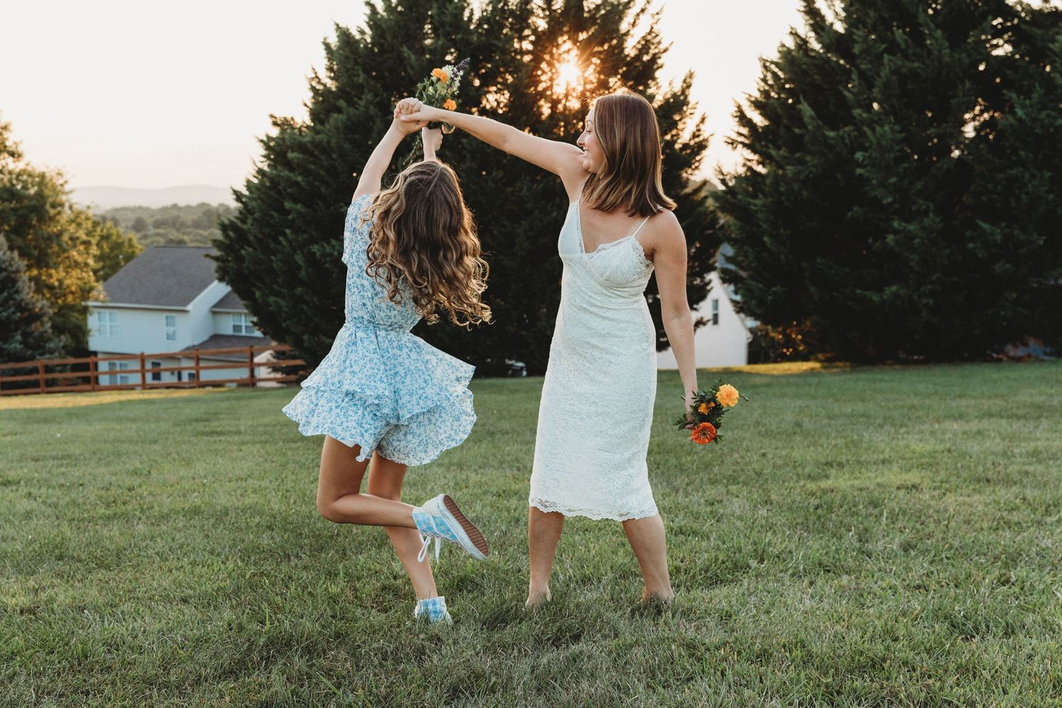 Playful bridesmaids in light blue dresses dancing on grassy hill at sunset.