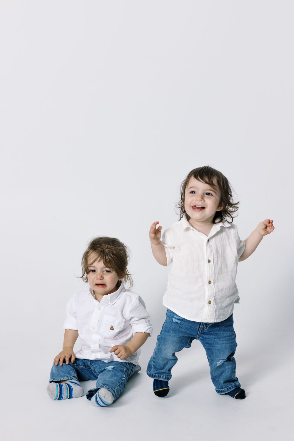 Two small children in white shirts and jeans playing against a light backdrop.