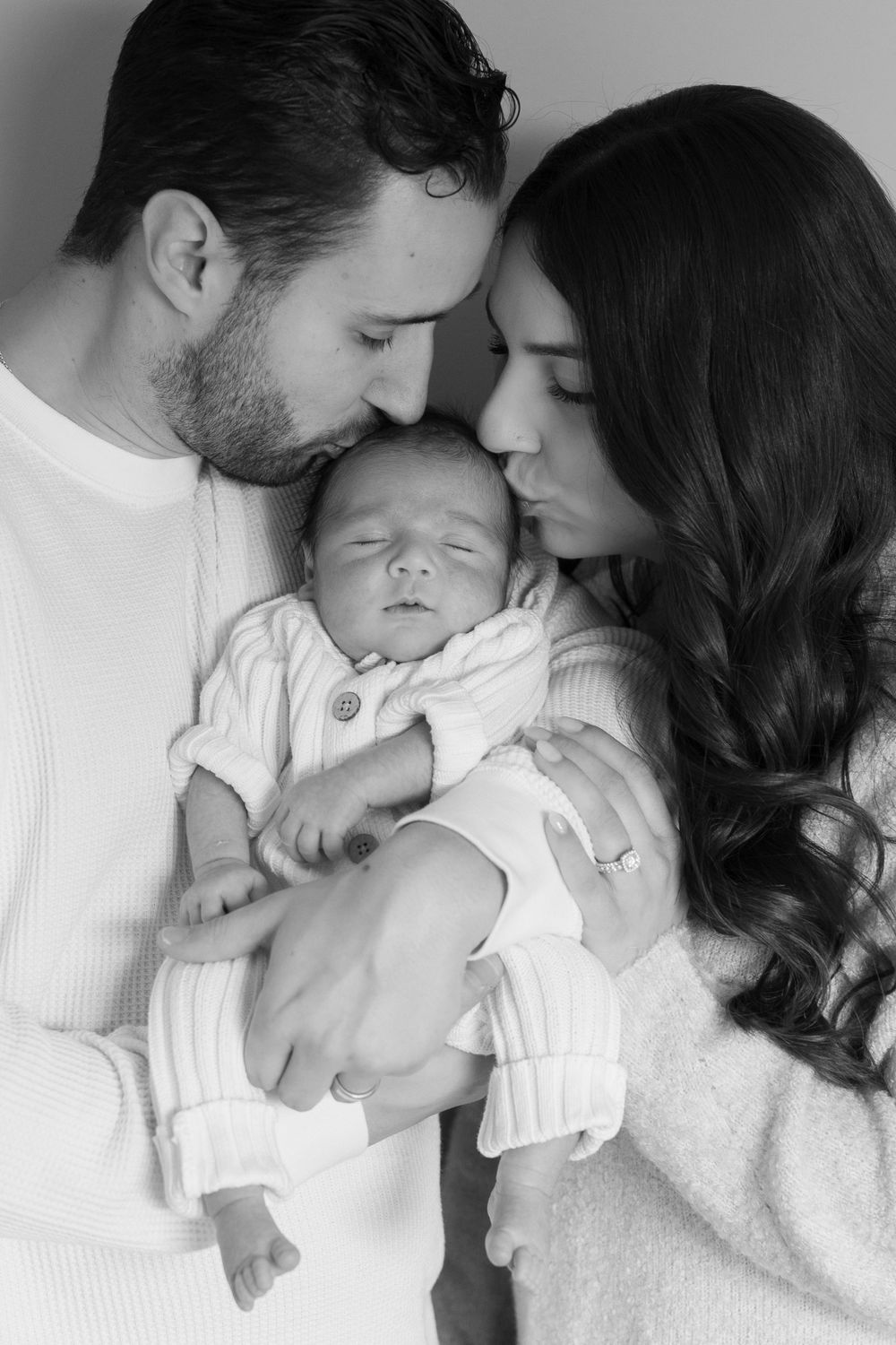 Parents sharing intimate moment with newborn baby in black and white portrait.
