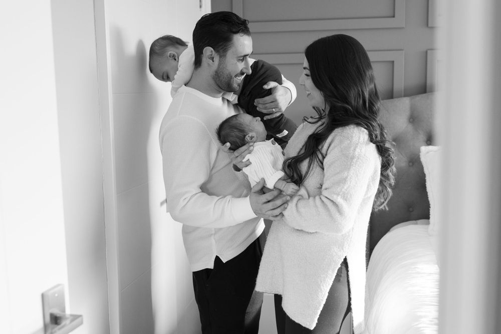 Parents in white sweaters holding newborn baby in bright room.