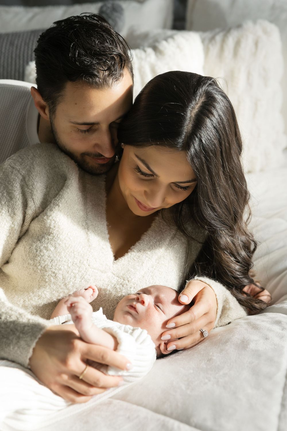 Parents in cozy sweaters snuggling with newborn on bed.