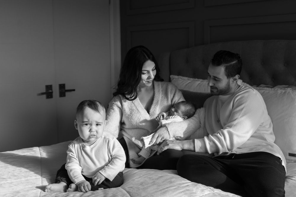 Family relaxing together on a bed in black and white.
