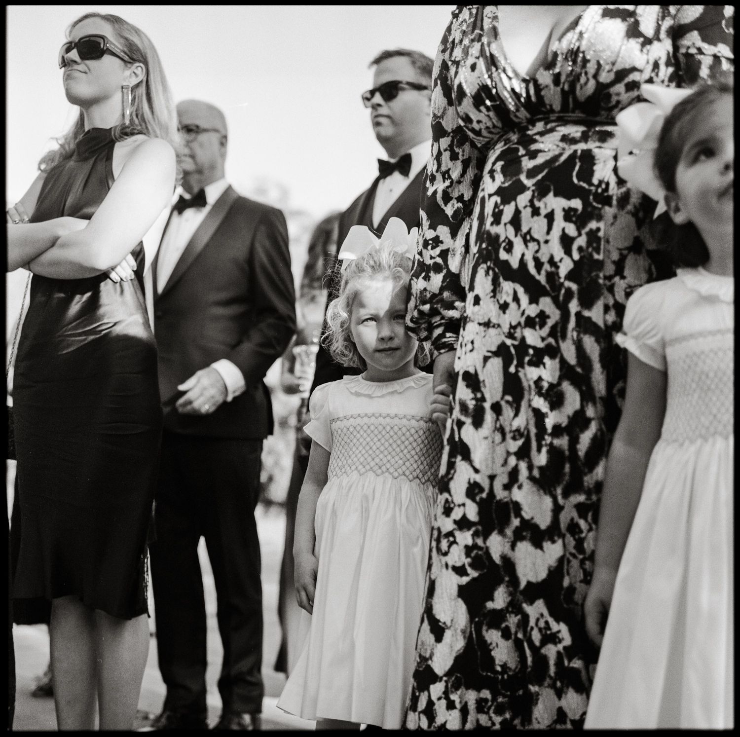 Flower girl is standing with family and looking right and the camera. It is a black and white film photo