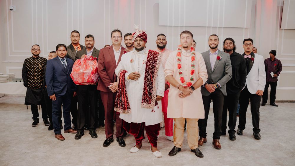 Wedding party members in formal suits and traditional South Asian attire pose for group photo.