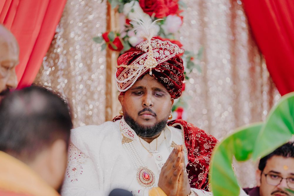 Traditional South Asian groom wearing white sherwani and red floral headpiece during ceremony.