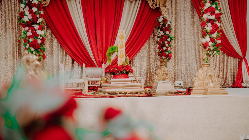 Elegant wedding stage decor with red drapes and floral arrangements in traditional style.