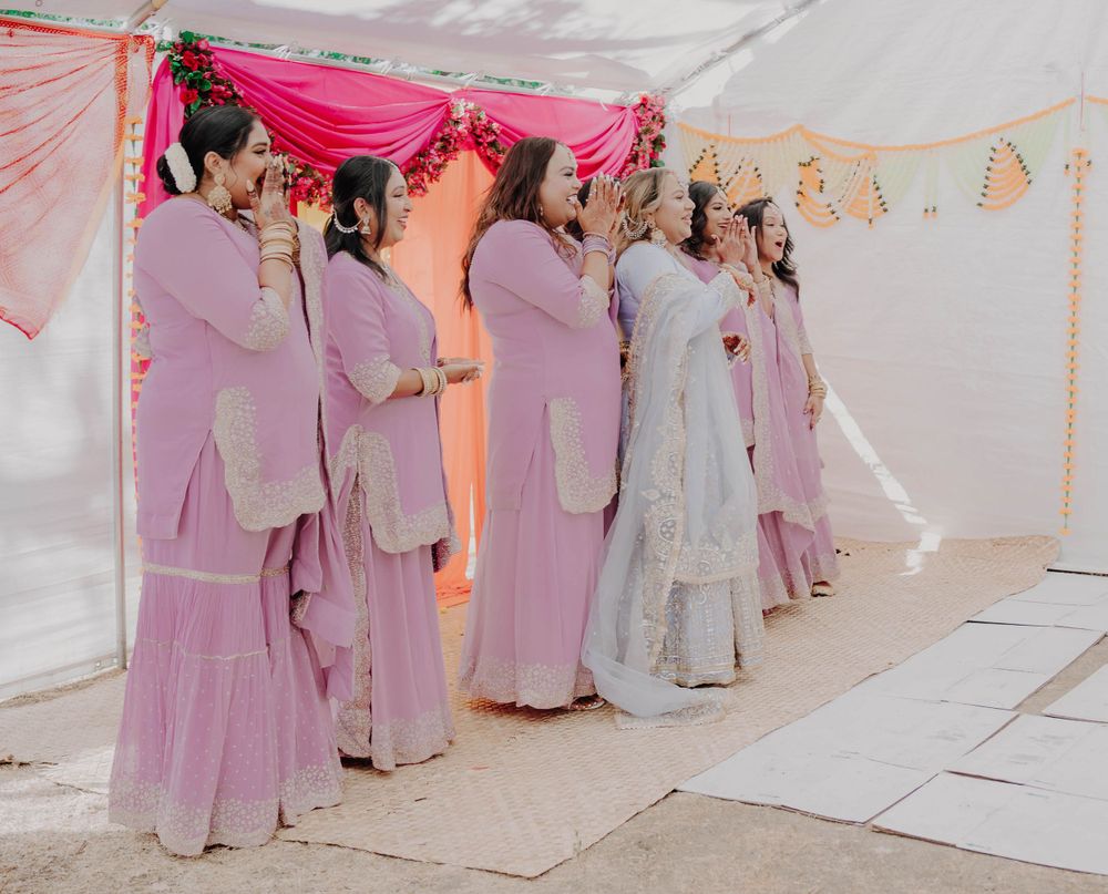 Wedding guests in pink traditional outfits forming a line under decorative tent.