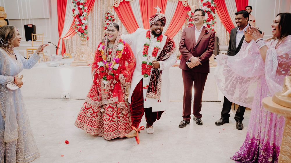 Traditional Indian wedding ceremony with red and white draped backdrop and floral decorations.