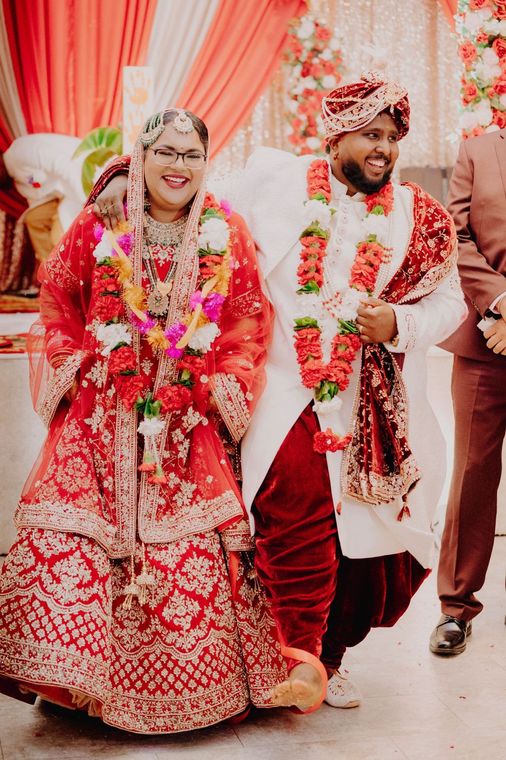 Couple in traditional red and white wedding attire during South Asian ceremony.