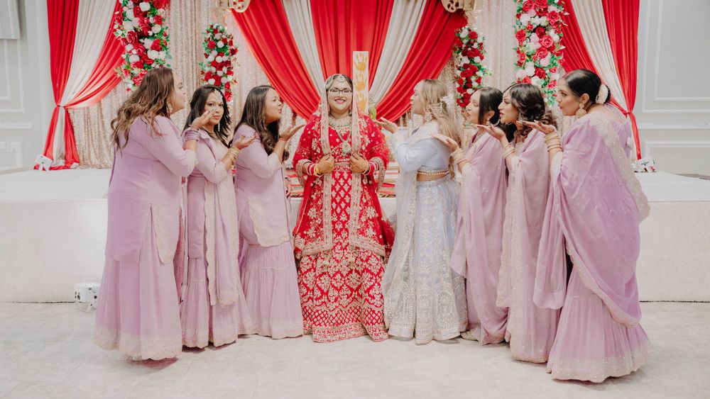 Wedding party dressed in pink outfits gathered around traditional red and white decorated mandap stage.