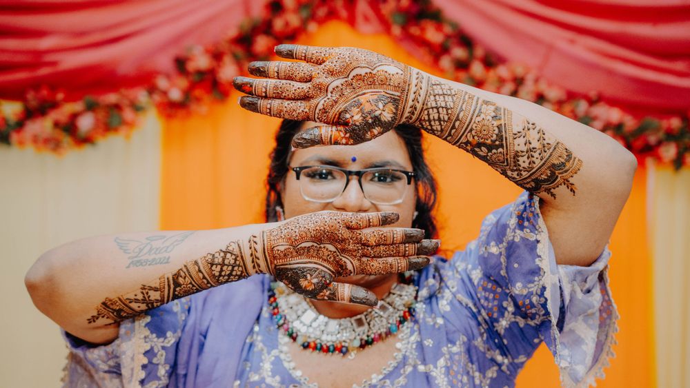 Intricate henna designs displayed on hands covering face with orange background.