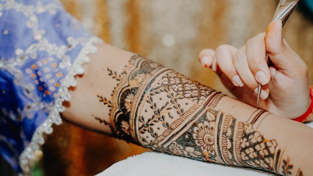 Detailed mehndi artwork being applied on arm with delicate patterns and designs.