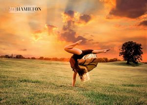 A graceful dancer performs a handstand against a dramatic orange sunset sky.