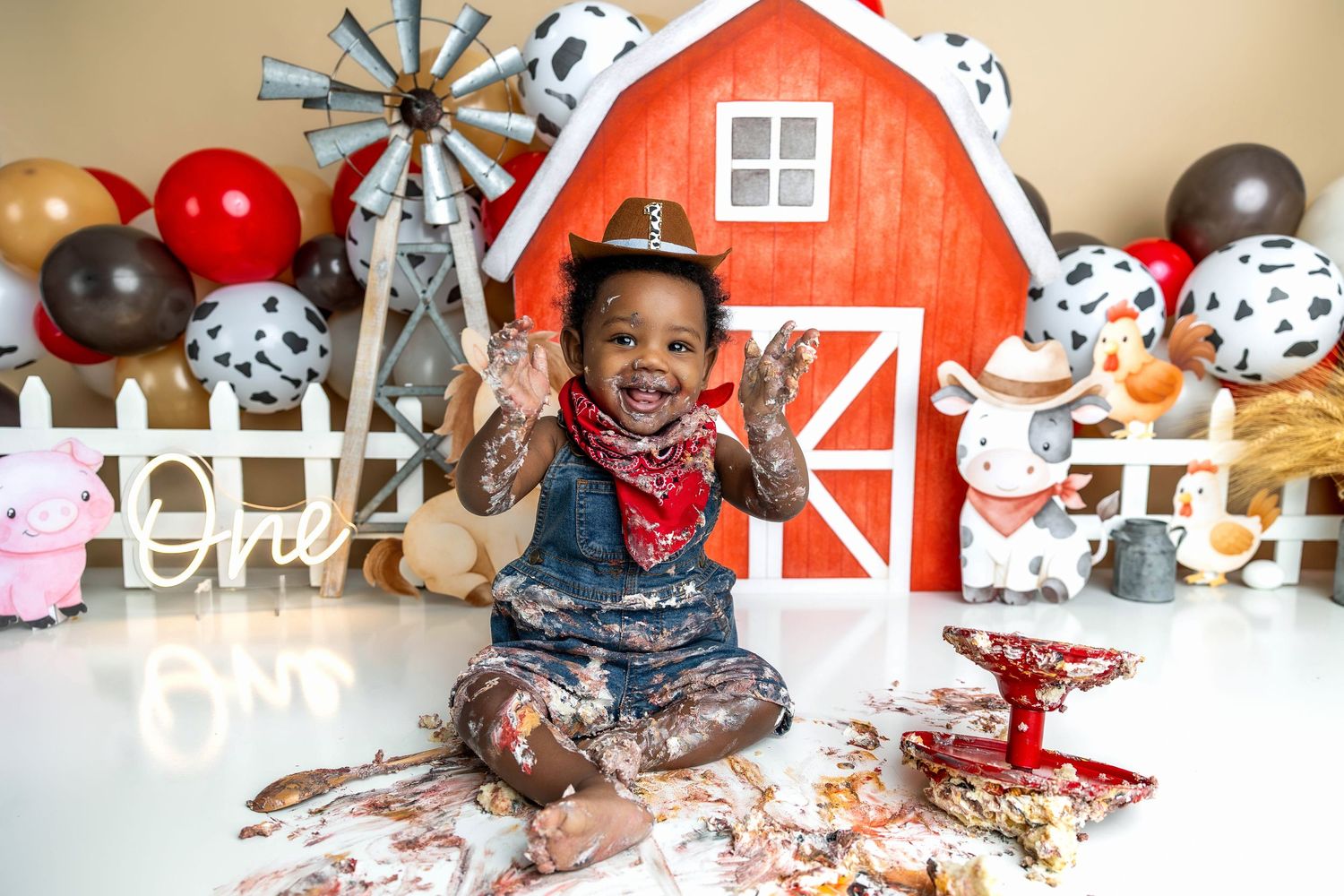 Baby in white outfit enjoying messy cake smash during first birthday photoshoot.