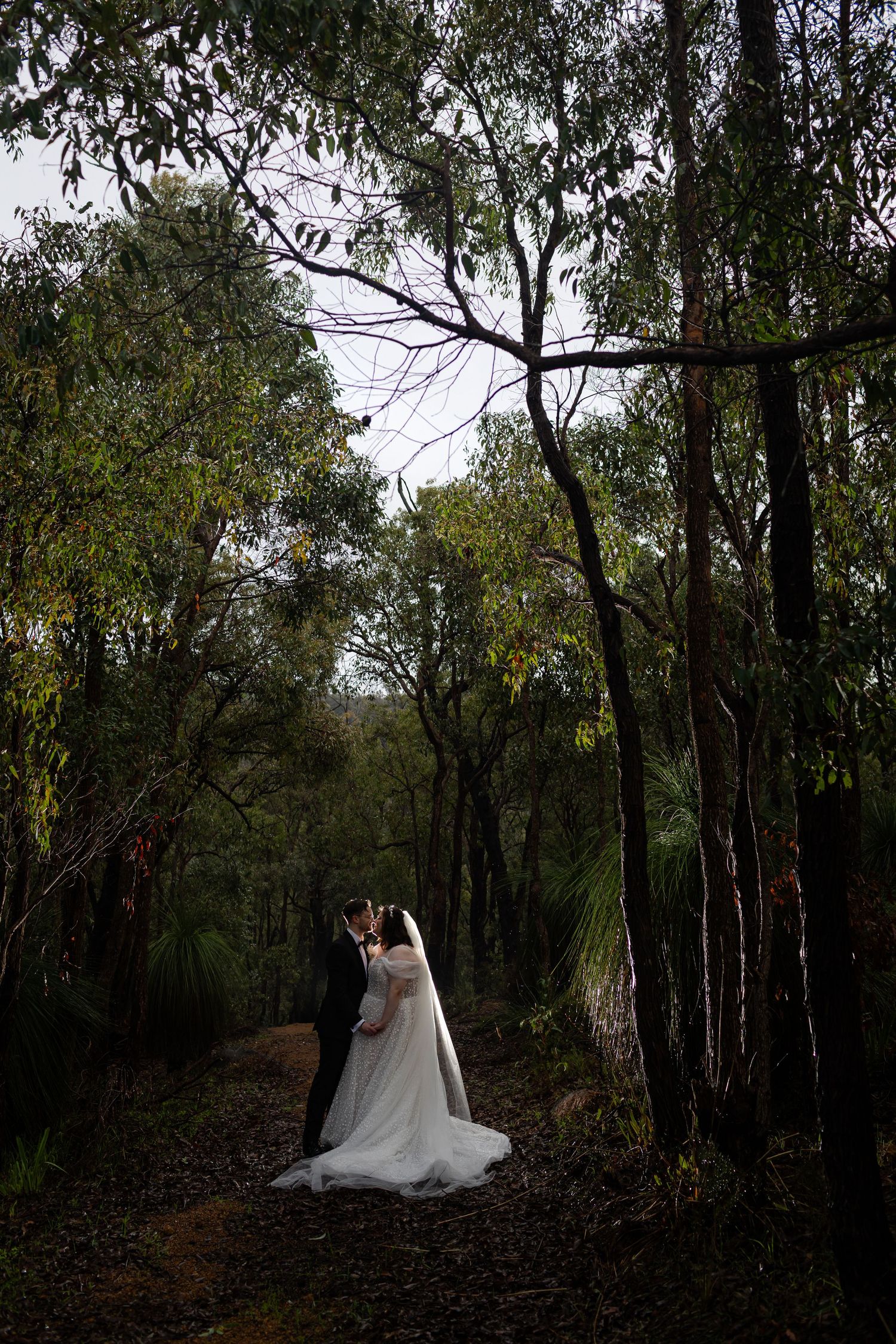 A romantic wedding couple poses with a vintage white car outside a stone church building.