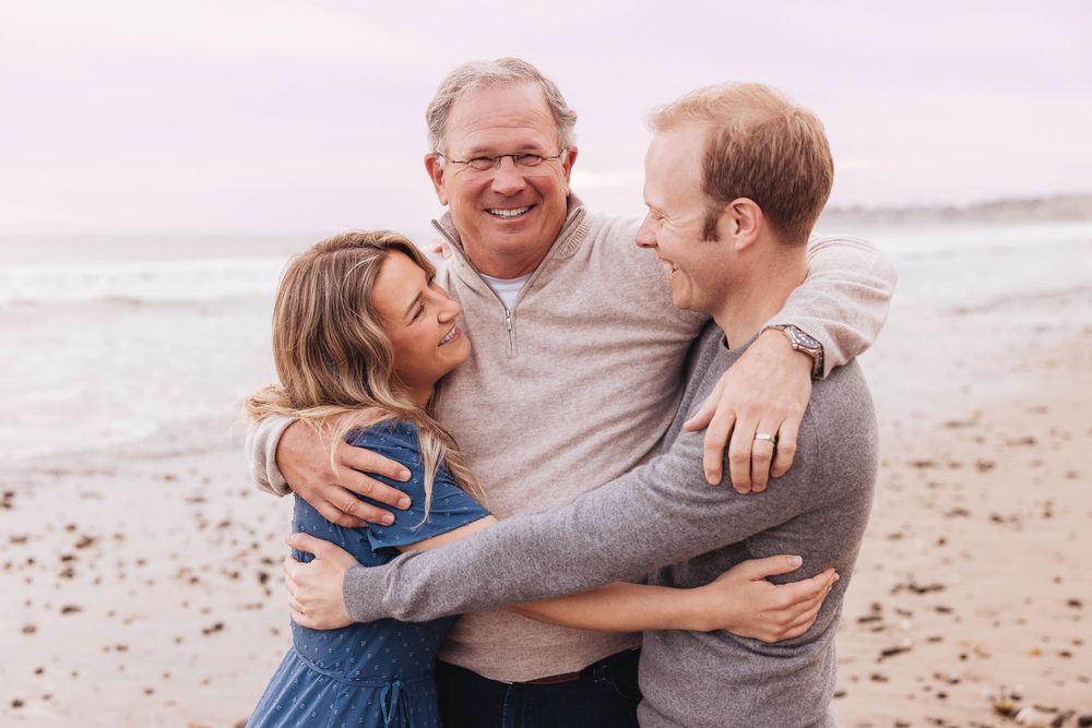 Three people share a joyful embrace while laughing together on a misty beach.