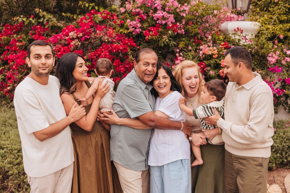 A group embraces warmly against a backdrop of vibrant pink bougainvillea flowers in an outdoor setting.