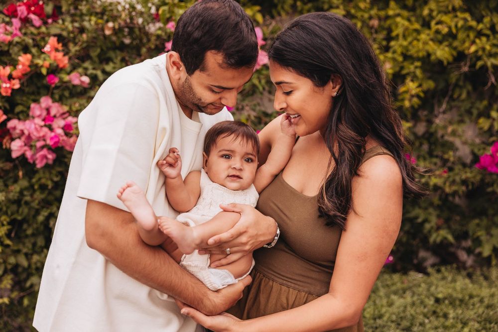 Family enjoying a tender moment together in a garden with pink flowers blooming in the background.