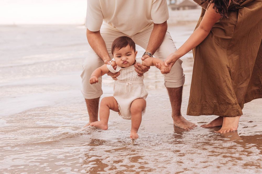 Family playing and splashing in shallow ocean water during sunset at the beach.