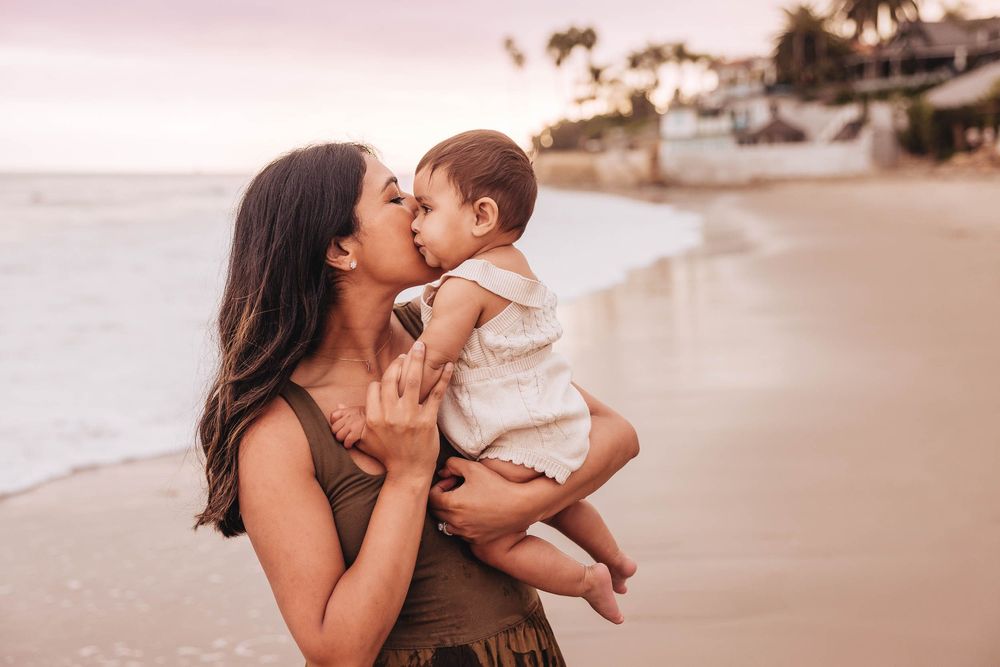 A tender moment between parent and baby on a sunset beach with palm trees in the background.