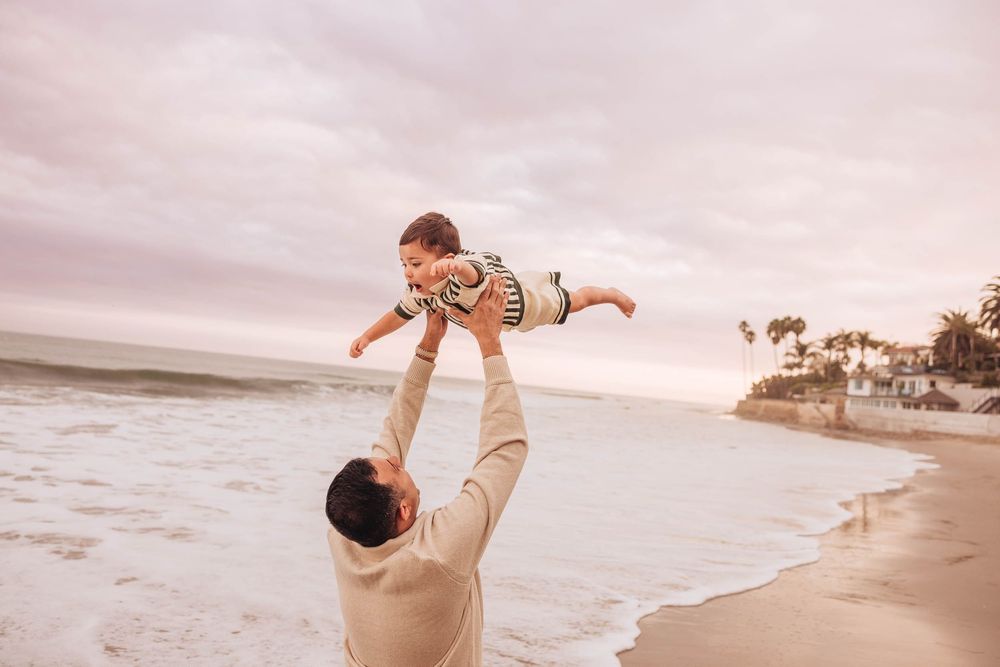 A joyful moment of a child being lifted high in the air at the beach during sunset.
