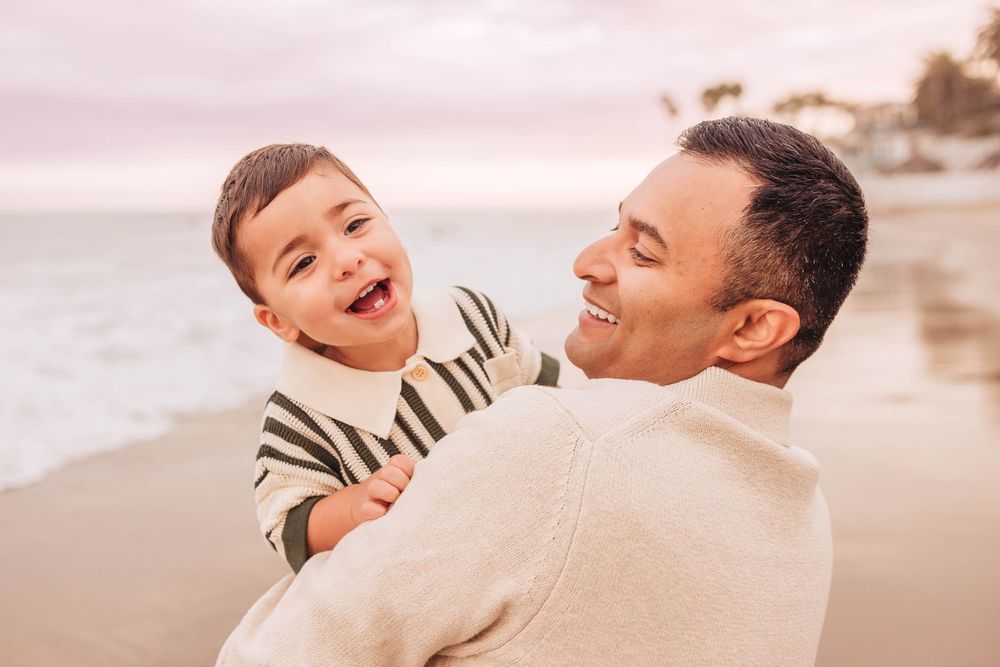 A family shares joyful embraces and laughter during a beach photoshoot at golden hour.