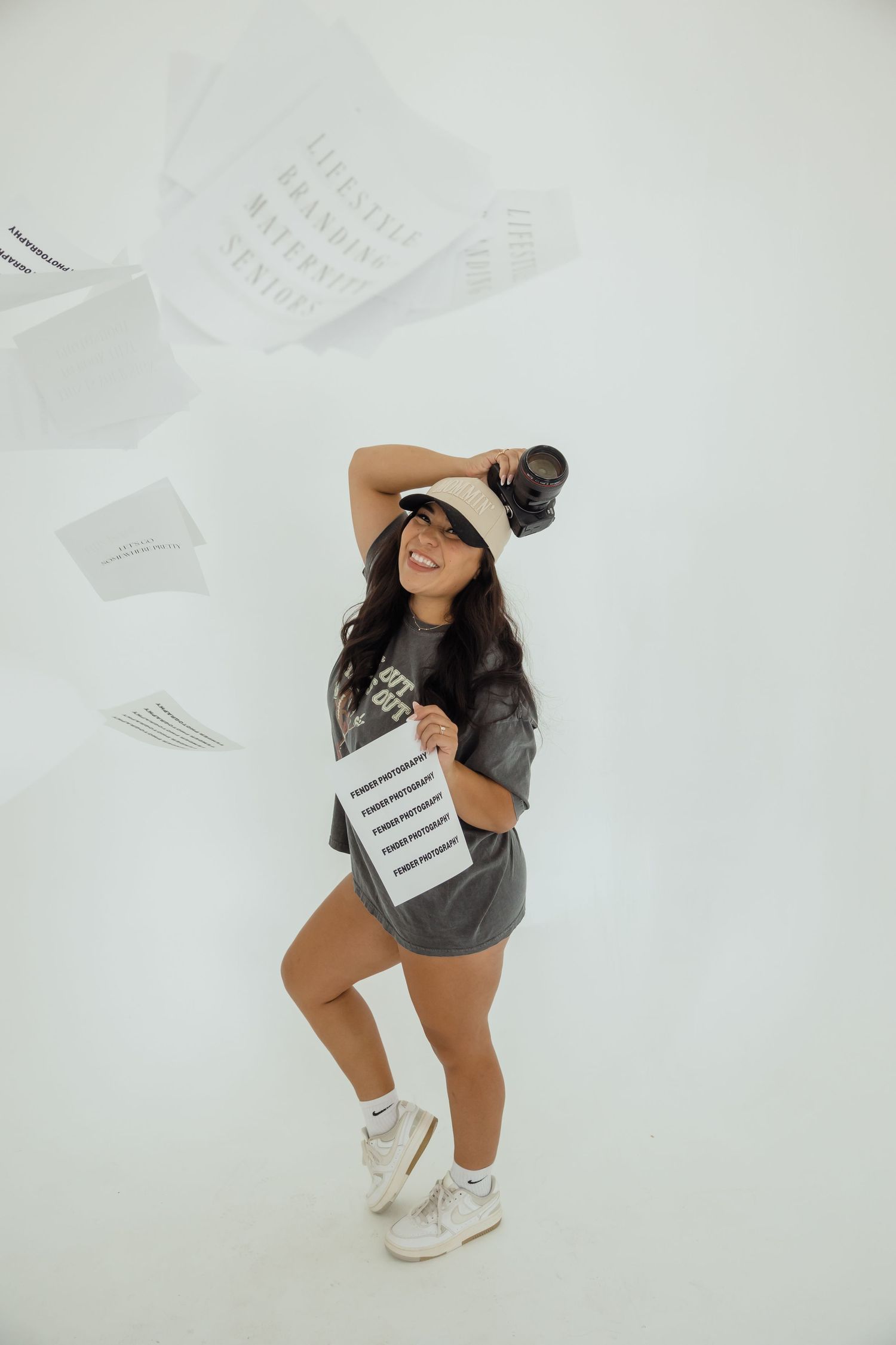 Smiling photographer holding camera and branded paper with pages flying in white studio.