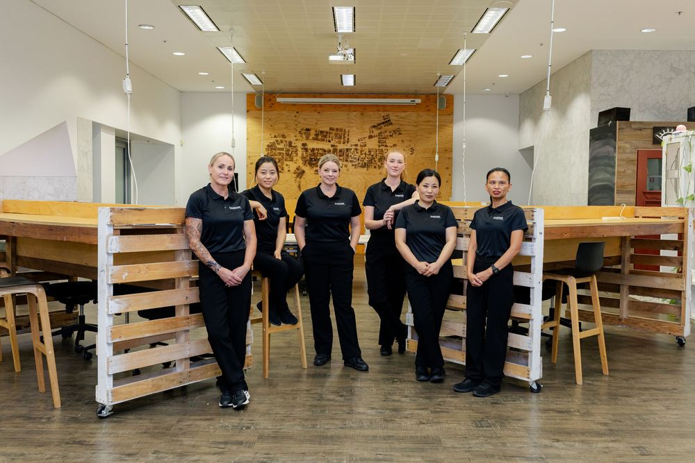 Healthcare workers in black uniforms move wooden furniture and equipment through a medical facility hallway.