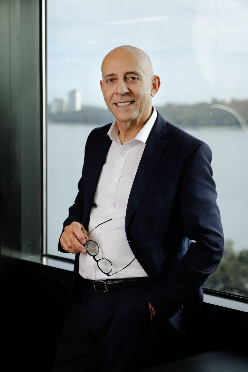 Professional portrait series of a businessman in a navy suit and white shirt seated by a window with city views.