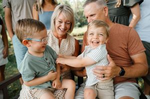 Grandparents laughing joyfully with two young grandsons on a sunny outdoor porch.