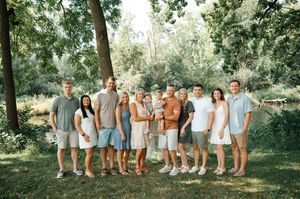 Large extended family group portrait standing together under shady trees outdoors in summer.