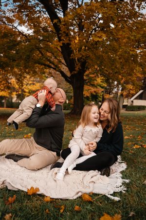 Happy family of four sitting on a blanket in a park during fall foliage season.