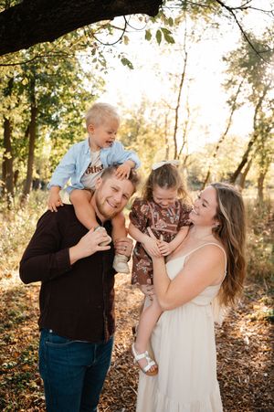 Happy family with two young children laughing together in a sunlit autumn forest.