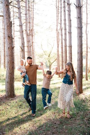Happy family walking hand-in-hand through sunlit pine forest with two boys.
