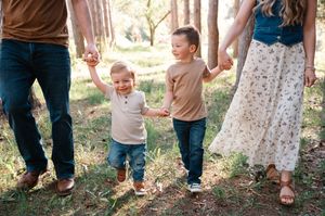 Two young brothers holding parents hands while walking in pine forest.