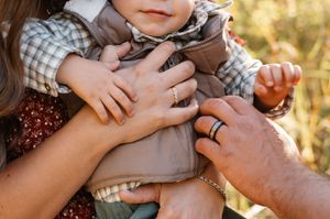 Parents lovingly holding their baby in a cozy plaid vest outdoors in fall.