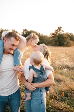 Young family with two children sharing a sweet kiss in a golden sunlit meadow.