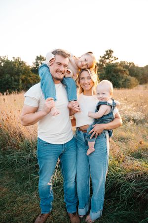 Smiling family of four posing together in a sunny golden field at sunset.