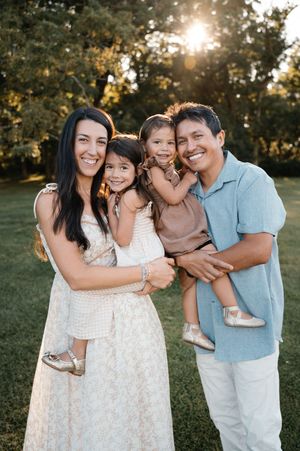Happy family of four smiling together in a lush green park at golden hour.