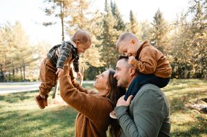 Joyful parents lifting their two young toddler sons outdoors in a sunny autumn park.