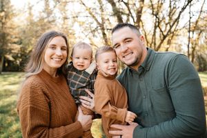 Smiling family of four with twin toddlers posing together outdoors in autumn foliage.