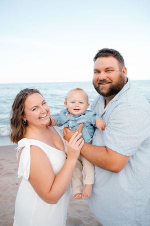 Happy family with smiling baby boy posing together on sandy beach.