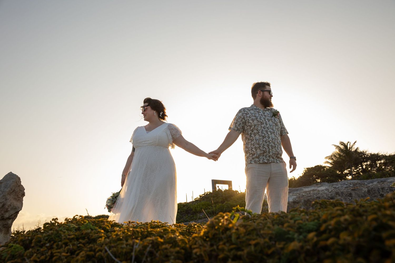 A couple holds hands while walking on rocky terrain at sunset.