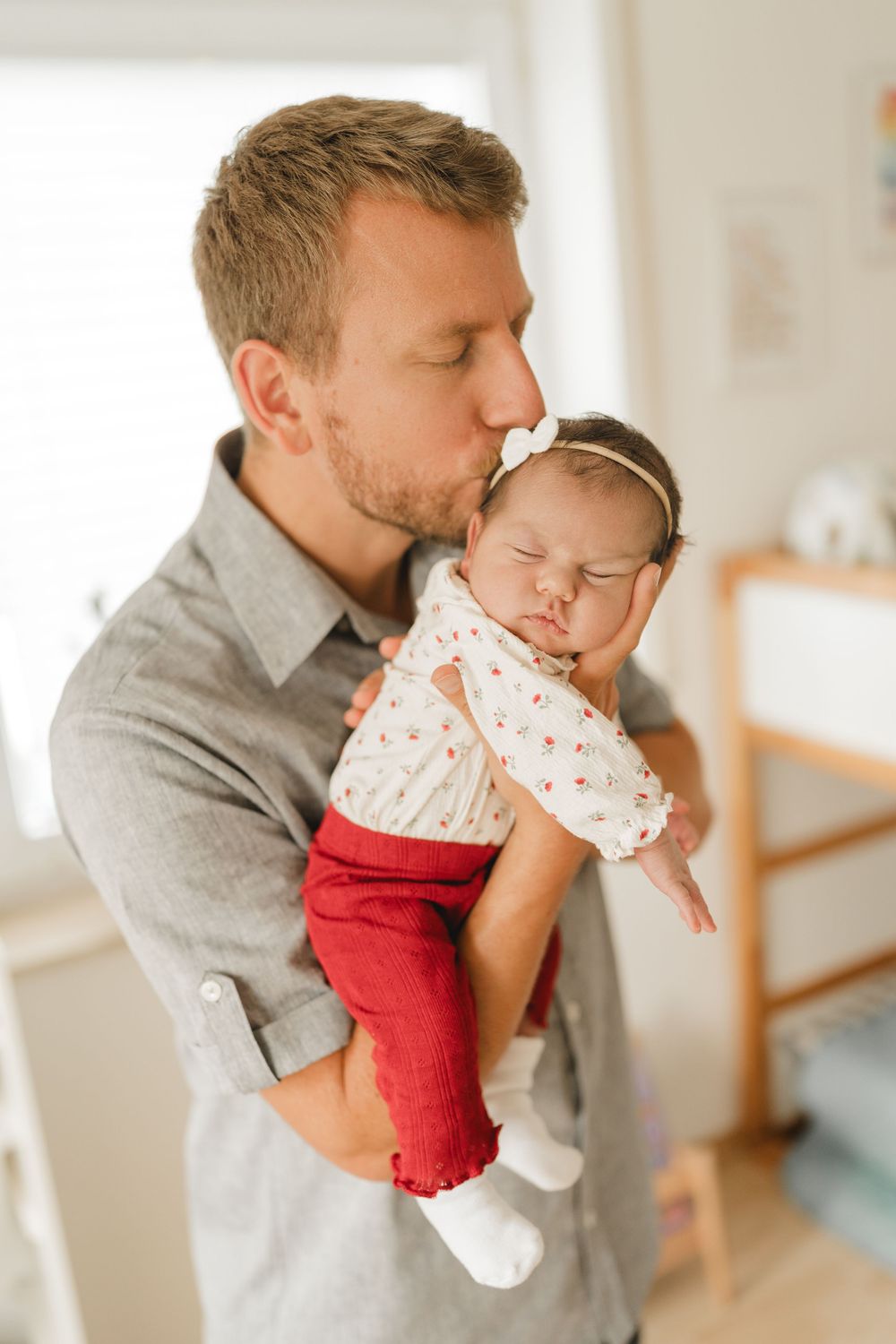 Papa küsst sein neugeborenes Baby auf dem Arm - Liebevolle Babyfotografie im eigenen Zuhause in Biberach von Ramona Maier