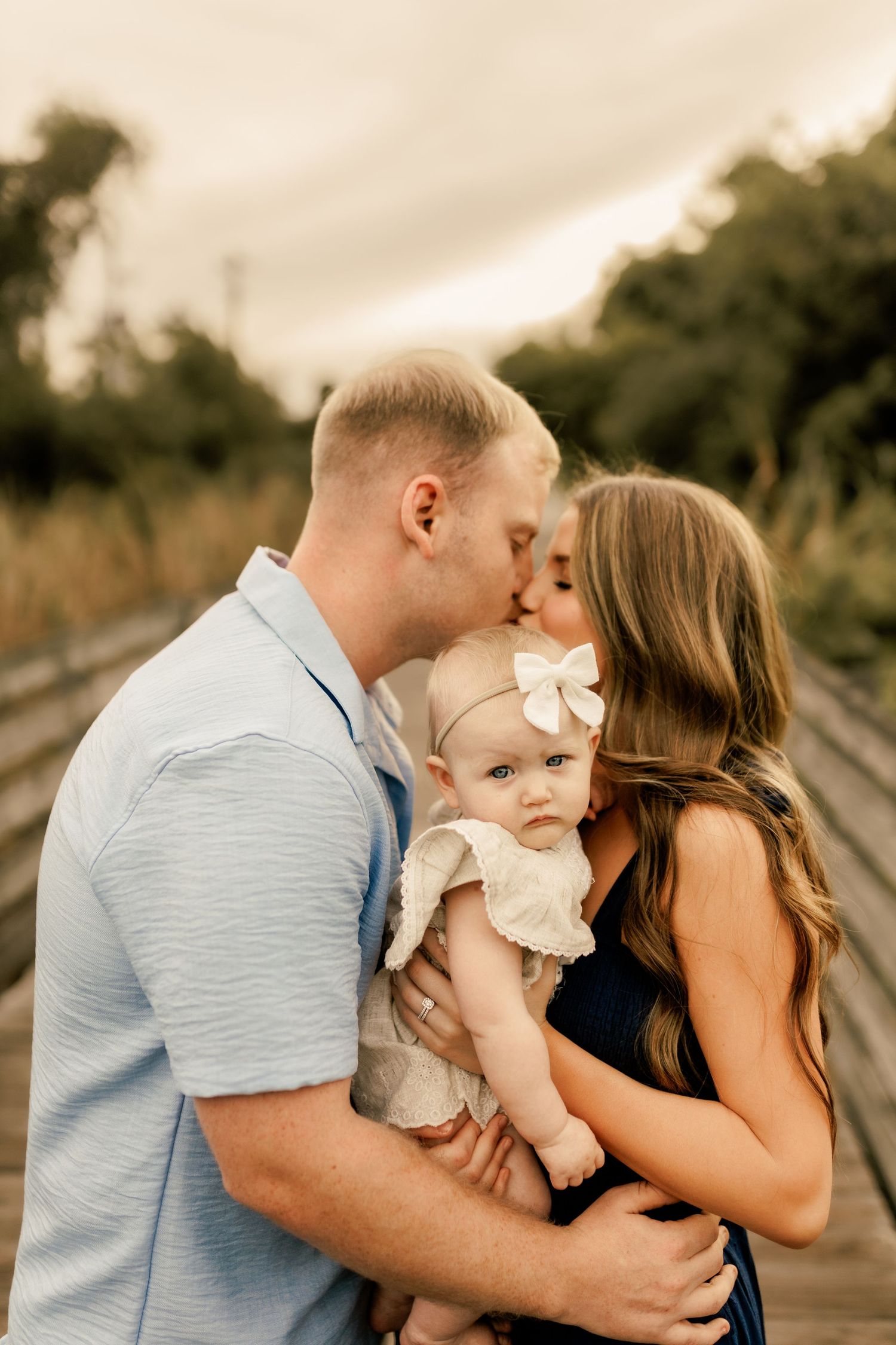 Family shares tender moment with baby outdoors during golden hour portrait session.