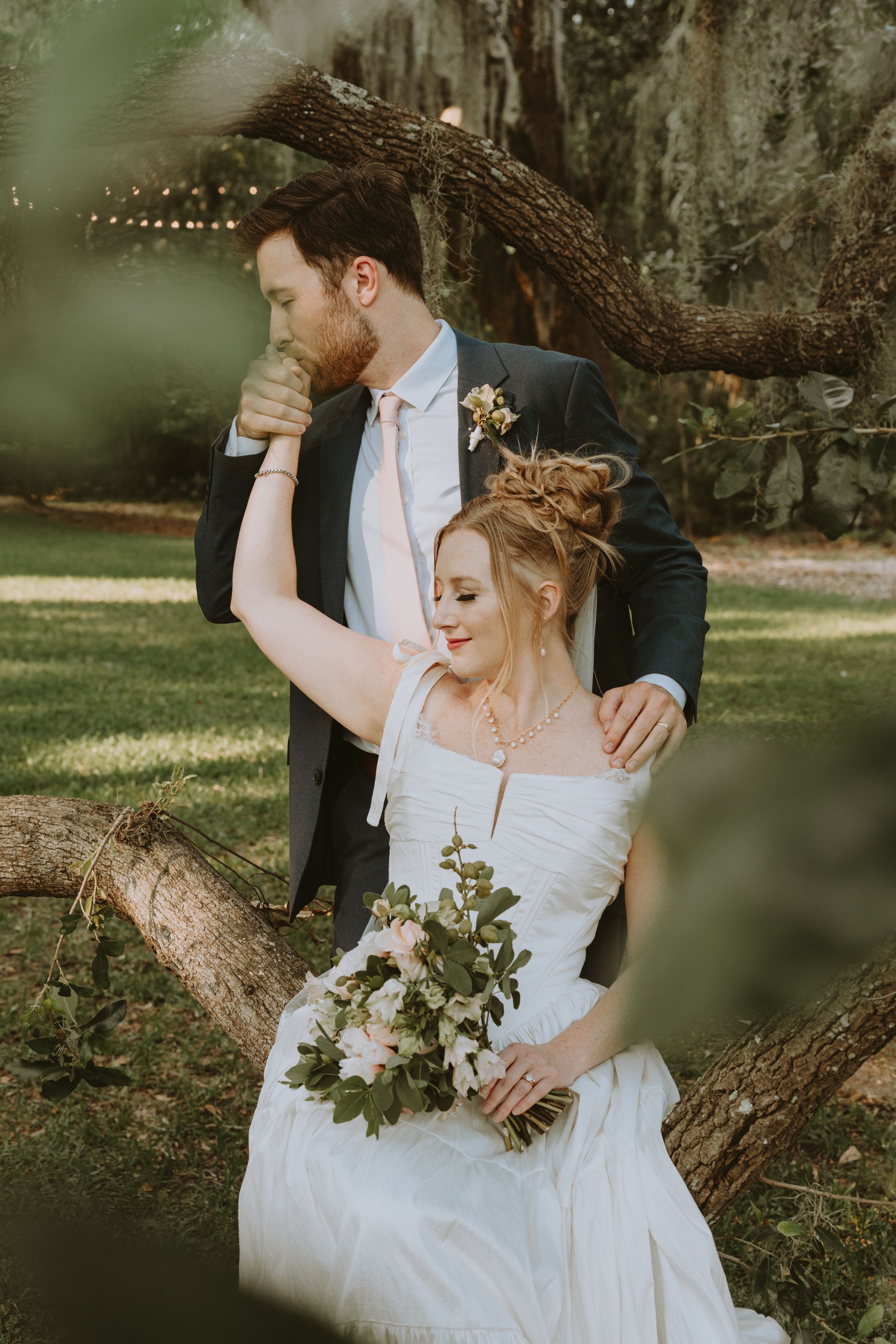 Wedding couple posing romantically under a large tree with white flowers.