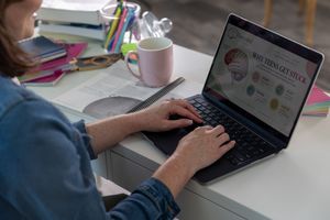 Woman typing on laptop displaying infographic about why teens get stuck, studying at a desk with books and a pink mug.